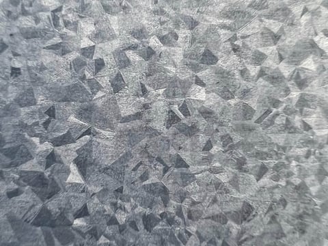 Close-up van een Aluzinc metalen plaat met een opvallende kristalstructuur, corrosiebestendig en ideaal voor dak- en gevelelementen