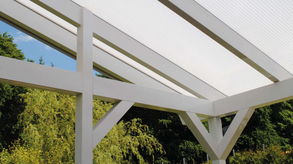 Witte kanaalplaten op een moderne terrasoverkapping met uitzicht op groene bomen op de achtergrond